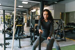 bonita hispânico jovem mulher fazendo alguns crossfit exercícios com uma corda às uma academia. foto