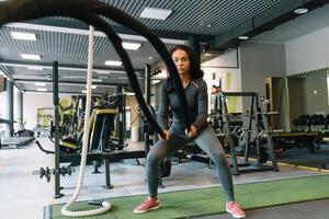 ginástica em a cordas. lindo fêmea dentro Academia trabalhando Fora com corda. jovem mulher Treinamento Difícil foto