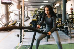 bonita hispânico jovem mulher fazendo alguns crossfit exercícios com uma corda às uma academia. foto