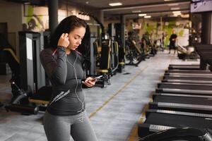 jovem mulher bebendo água e levando uma pausa depois de exercite-se dentro Academia foto