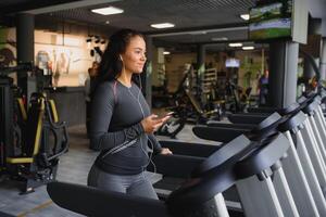 jovem em forma mulher corrida em esteira ouvindo para música através da fone de ouvido às academia. conceito do saudável estilo de vida foto