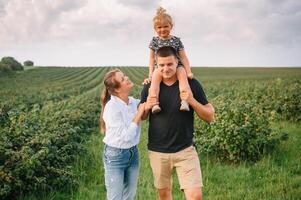 feliz família caminhando dentro a parque. mãe, Papai e filha andar ao ar livre, pais segurando a bebê garotas mãos. infância, paternidade, família títulos, casamento conceito. foto