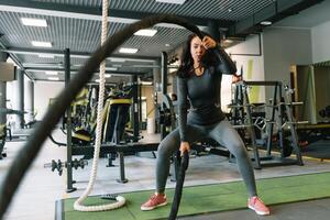 bonita hispânico jovem mulher fazendo alguns crossfit exercícios com uma corda às uma academia. foto