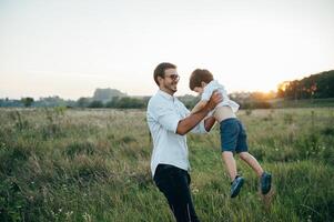 bonito Papai com dele pequeno fofa filho estão tendo Diversão e jogando em verde gramíneo grama. feliz família conceito. beleza natureza cena com família ao ar livre estilo de vida. família em repouso junto. pais dia. foto