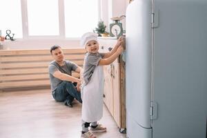 jovem homem e dele filho com forno Folha dentro cozinha. pai com pequeno filho em a cozinha. foto