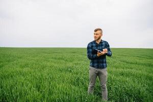 jovem agrônomo detém caderno dentro verde trigo campo. agronegócio conceito. agrícola engenheiro em pé dentro uma trigo campo com uma tábua dentro verão. foto