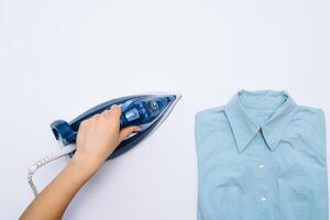 fêmea mão passar roupa roupas topo Visão isolado em branco fundo. jovem mulher com ferro passar roupa do homem camisa visto a partir de acima durante tarefas domésticas. azul ferro em branco mesa foto