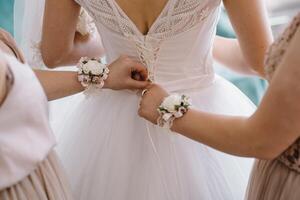 dama de honra preparando noiva para Casamento dia. dama de honra ajudando noiva apertar laço dela Casamento branco vestir antes cerimônia. luxo nupcial vestir fechar acima. Casamento manhã momentos detalhes conceito. foto