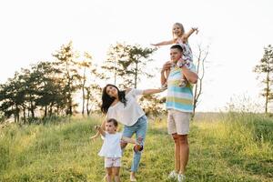 cor foto do sorridente jovem pais e dois crianças, descansar e ter Diversão dentro natureza. amor, família e feliz infância estilo de vida conceito.