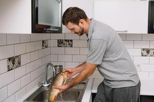 homem corte fresco peixe dentro cozinha dentro lar. homem açougueiro peixe para cozinhar. foto