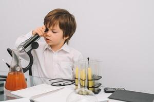 a Garoto com uma microscópio e vários colorida frascos em uma branco fundo. uma Garoto fazendo experimentos dentro a laboratório. explosão dentro a laboratório. Ciência e Educação. foto