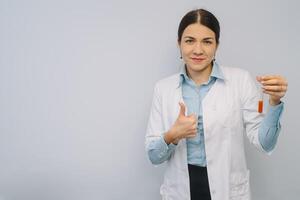 fêmea médico dentro branco uniforme é segurando frascos enquanto em pé contra branco fundo. foto