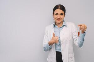 fêmea médico dentro branco uniforme é segurando frascos enquanto em pé contra branco fundo. foto