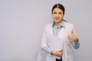 fêmea médico dentro branco uniforme é segurando frascos enquanto em pé contra branco fundo foto