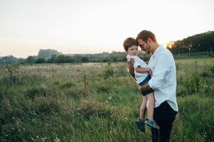 bonito Papai com dele pequeno fofa filho estão tendo Diversão e jogando em verde gramíneo grama. feliz família conceito. beleza natureza cena com família ao ar livre estilo de vida. família em repouso junto. pais dia. foto