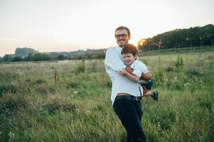 bonito Papai com dele pequeno fofa filho estão tendo Diversão e jogando em verde gramíneo grama. feliz família conceito. beleza natureza cena com família ao ar livre estilo de vida. família em repouso junto. pais dia. foto