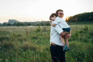 bonito Papai com dele pequeno fofa filho estão tendo Diversão e jogando em verde gramíneo grama. feliz família conceito. beleza natureza cena com família ao ar livre estilo de vida. família em repouso junto. pais dia. foto