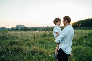 bonito Papai com dele pequeno fofa filho estão tendo Diversão e jogando em verde gramíneo grama. feliz família conceito. beleza natureza cena com família ao ar livre estilo de vida. família em repouso junto. pais dia. foto