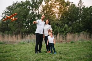 pai, mãe e filho jogando com brinquedo avião dentro a parque. amigáveis família. pessoas tendo Diversão ao ar livre. cenário fez em a fundo do a parque e azul céu. conceito do uma feliz família foto