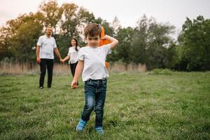 pai, mãe e filho jogando com brinquedo avião dentro a parque. amigáveis família. pessoas tendo Diversão ao ar livre. cenário fez em a fundo do a parque e azul céu. conceito do uma feliz família foto