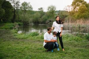 feliz família mãe pai e criança filho em natureza em pôr do sol. mãe, Papai e criança rindo e abraçando, desfrutando natureza fora. ensolarado dia, Boa humor. conceito do uma feliz família. foto