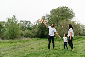 pai, mãe e filho jogando com brinquedo avião dentro a parque. amigáveis família. pessoas tendo Diversão ao ar livre. cenário fez em a fundo do a parque e azul céu. conceito do uma feliz família foto