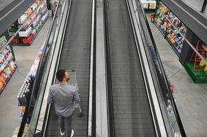 uma homem com uma compras carrinho em a escada rolante dentro uma hardware loja. foto