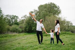 pai, mãe e filho jogando com brinquedo avião dentro a parque. amigáveis família. pessoas tendo Diversão ao ar livre. cenário fez em a fundo do a parque e azul céu. conceito do uma feliz família foto