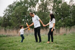 pai, mãe e filho jogando com brinquedo avião dentro a parque. amigáveis família. pessoas tendo Diversão ao ar livre. cenário fez em a fundo do a parque e azul céu. conceito do uma feliz família foto