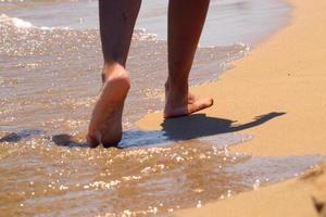 mulher caminhando descalça na areia deixando pegadas na praia dourada. Pernas femininas caminham à beira-mar. férias, férias de verão ou conceito de férias. pés descalços de uma mulher caminhando ao longo de uma praia arenosa. foto