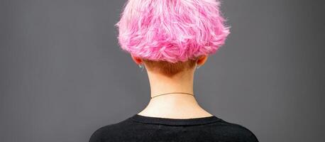 costas do fêmea cabeça com encaracolado curto Rosa cabelo contra a Sombrio fundo. foto