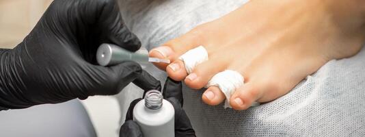 pedicure aplicando transparente verniz para a fêmea unhas dos pés dentro uma beleza salão. foto