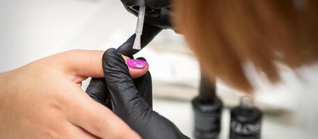 pintura unhas do uma mulher. mãos do manicuro dentro Preto luvas aplicando Rosa unha polonês em fêmea unhas dentro uma beleza salão. foto