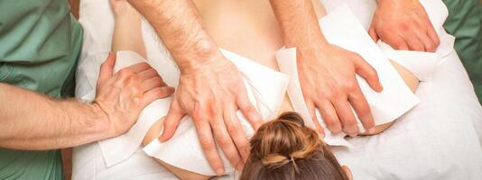 costas massagem com quatro mãos dentro a spa salão. dois massagem terapeutas faço uma costas massagem para uma jovem mulher. foto