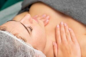 massageando fêmea peito. jovem lindo caucasiano mulher com fechadas olhos obtendo peito massagem às beleza spa salão. foto