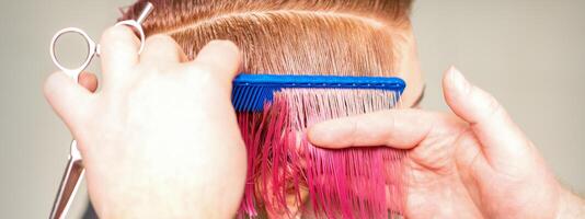 mãos do cabeleireiro pentear cabelo fazer curto Rosa Penteado para uma jovem caucasiano mulher dentro uma beleza salão. foto