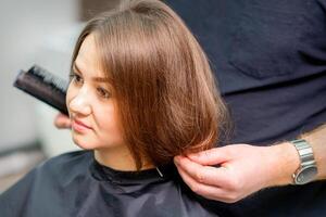 estilo fêmea cabelo. masculino cabeleireiro faz Penteado para uma jovem mulher dentro uma beleza salão. foto