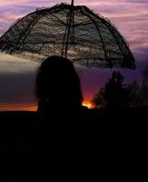 mulher com uma renda guarda-chuva dentro a pôr do sol foto