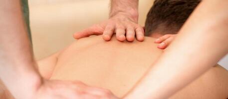 jovem homem recebendo costas massagem dentro quatro mãos dentro spa beleza salão. foto