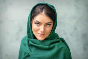 retrato do uma bonita jovem caucasiano mulher com Maquiagem dentro uma verde lenço de cabeça em cinzento fundo. foto