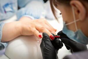 pintura unhas do uma mulher. mãos do manicuro dentro Preto luvas aplicando vermelho unha polonês em fêmea unhas dentro uma beleza salão. foto