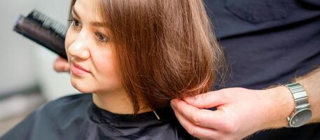 estilo fêmea cabelo. masculino cabeleireiro faz Penteado para uma jovem mulher dentro uma beleza salão. foto