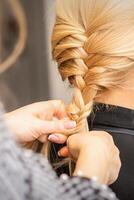 trança trança. mãos do fêmea cabeleireiro tranças grandes trança para uma Loiras mulher dentro uma cabelo salão. foto