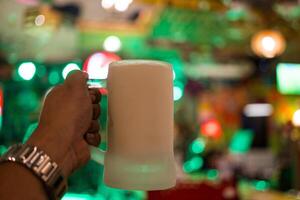 mão segurando Cerveja dentro uma congeladas vidro com bar luz borrão fundo foto