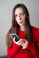 lindo jovem mulher com azul olhos e grandes cabelo dentro uma lindo Jaqueta relógios a notícia em a telefone foto