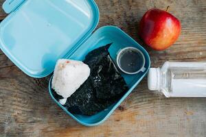 ásia estudante lancheira do onigiri, maçã e soja molho com garrafa do água, em de madeira fundo foto