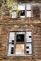 abandonado de madeira casa com quebrado janelas, embarcado acima portas, e cheio com hera. foto