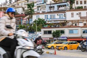 Fethiye, Peru - dezembro 8, 2022. homem em lambreta passeios através limitar rua dentro pequeno Cidade com lojas e cafés em ambos lados. foto