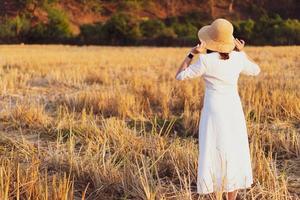 retrato de uma jovem com chapéu de palha e vestido branco em pé no arrozal seco ao pôr do sol foto