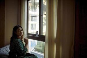 Mulher asiática sentada ao lado da janela com videochamada em smartphone ligada foto